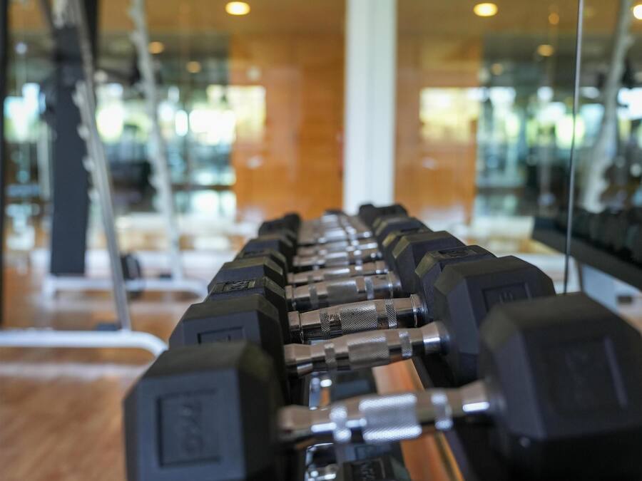 Eine Reihe von Hanteln in einem Fitnessstudio mit Spiegelwänden und Holzboden.