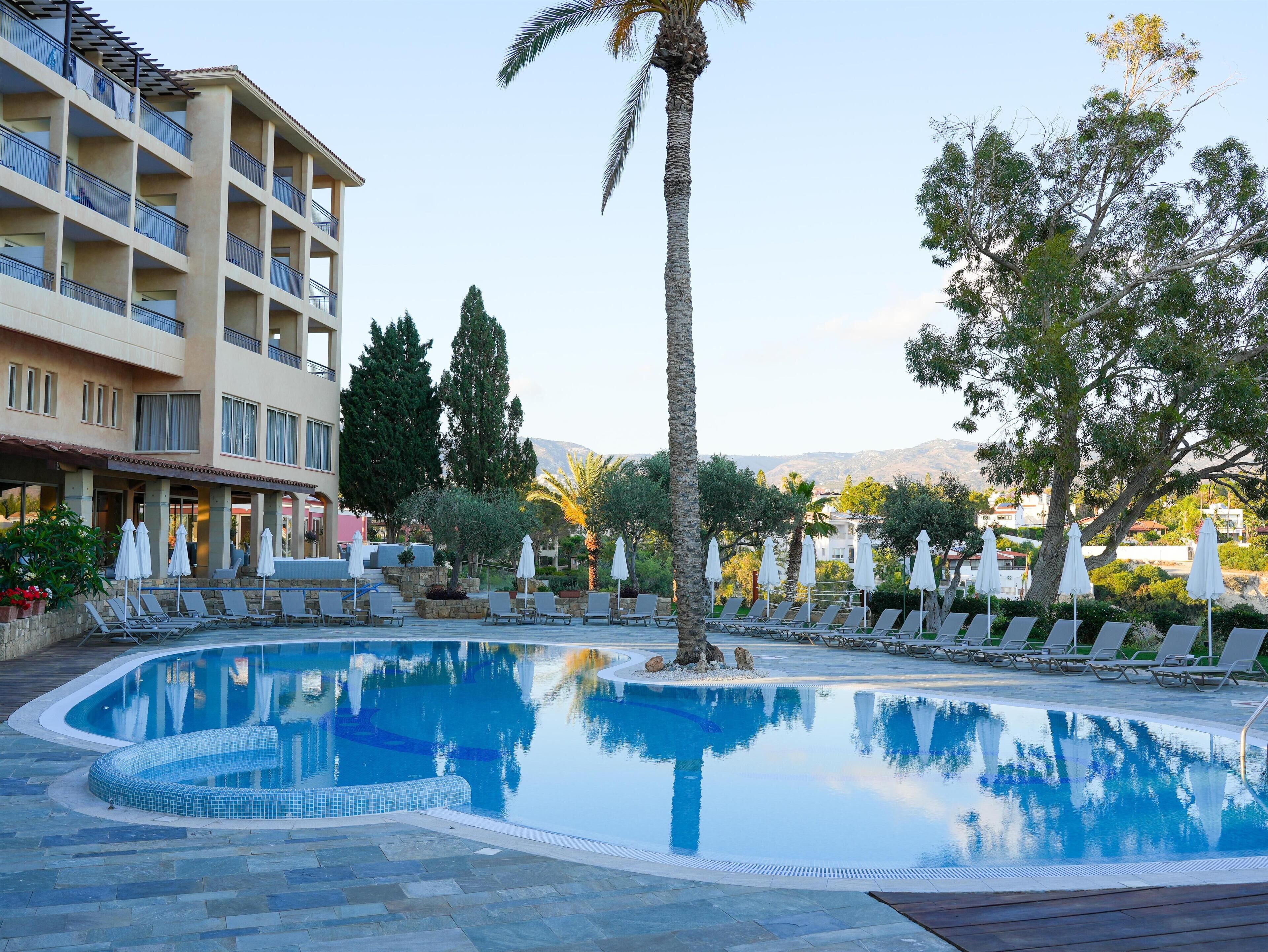 A pool area with lounge chairs and umbrellas, surrounded by trees and a building with balconies.