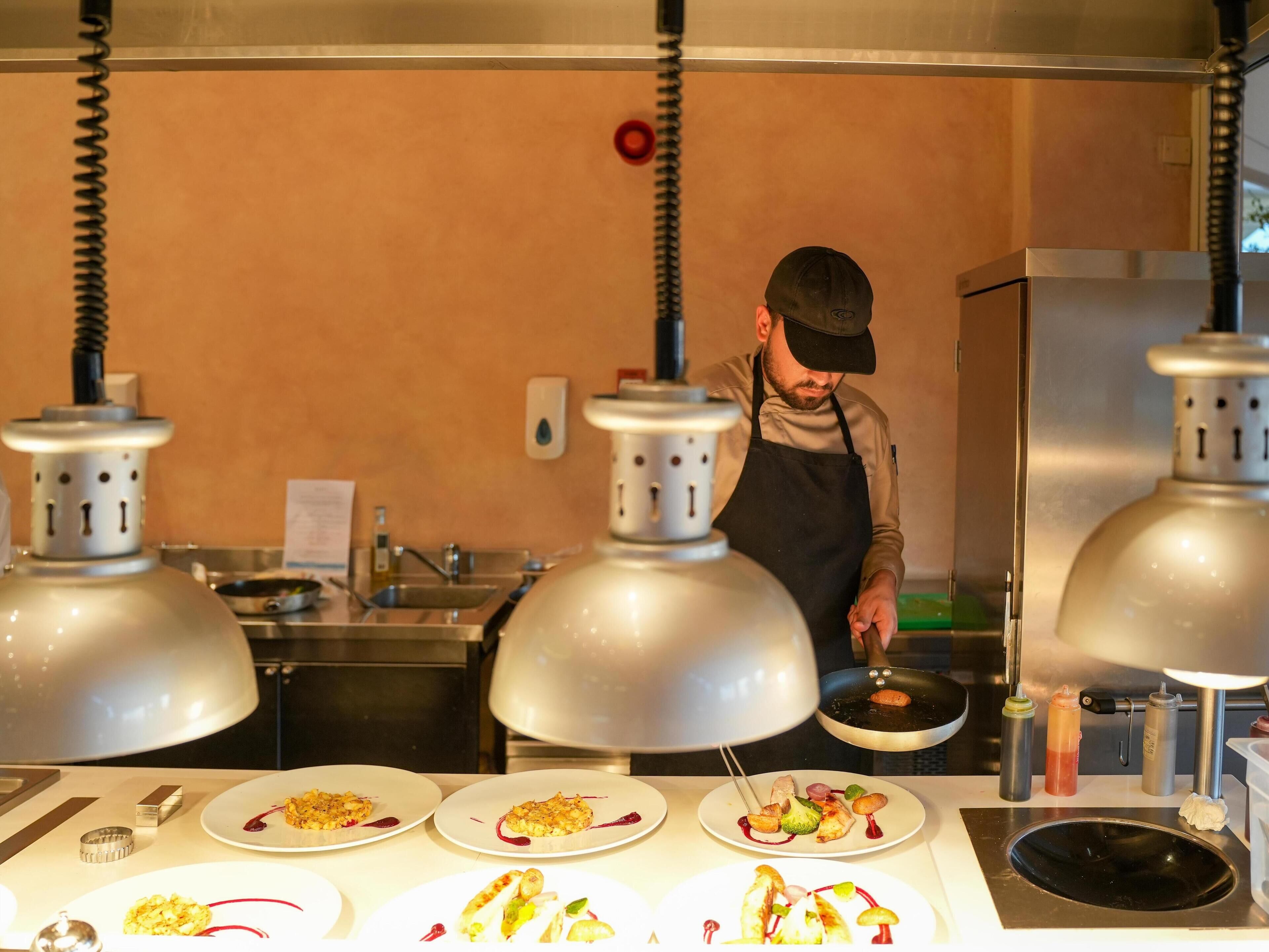A chef preparing food in a kitchen with stainless steel appliances and a white countertop.