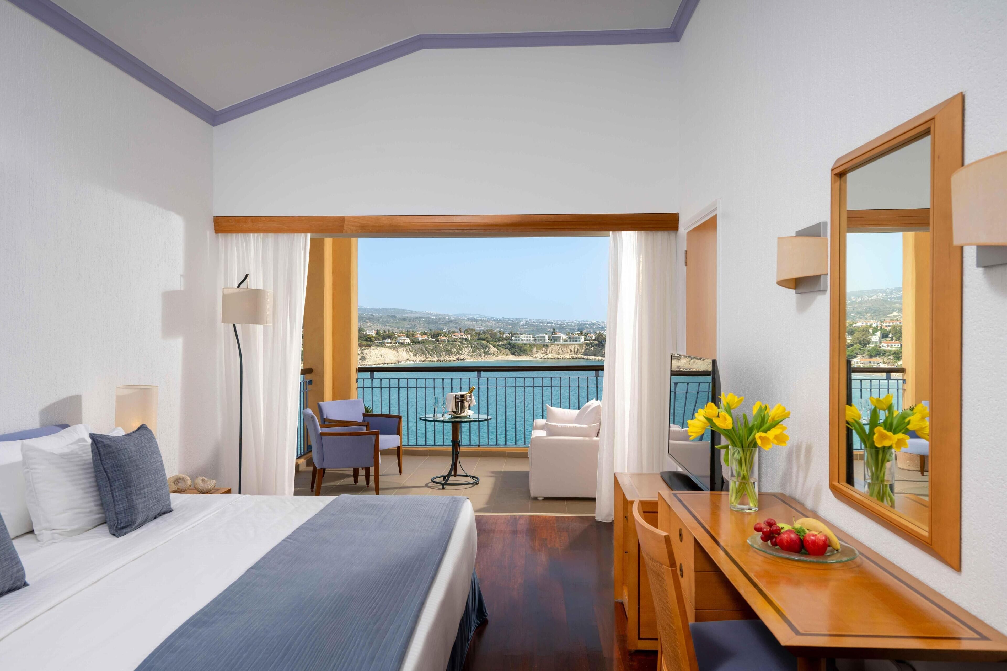 Habitación de hotel con cama, escritorio, silla, mesita y vista al mar.