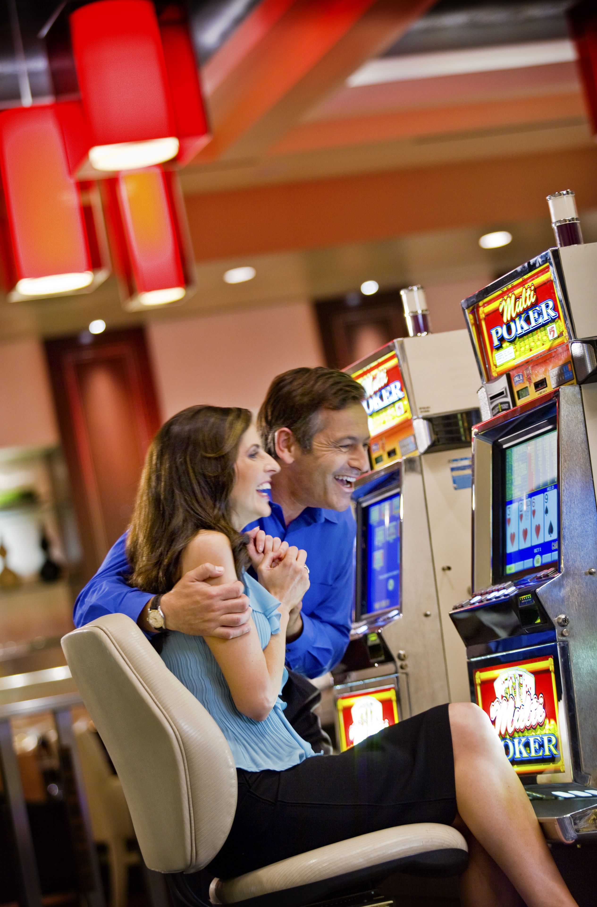 A couple playing poker at a casino machine.