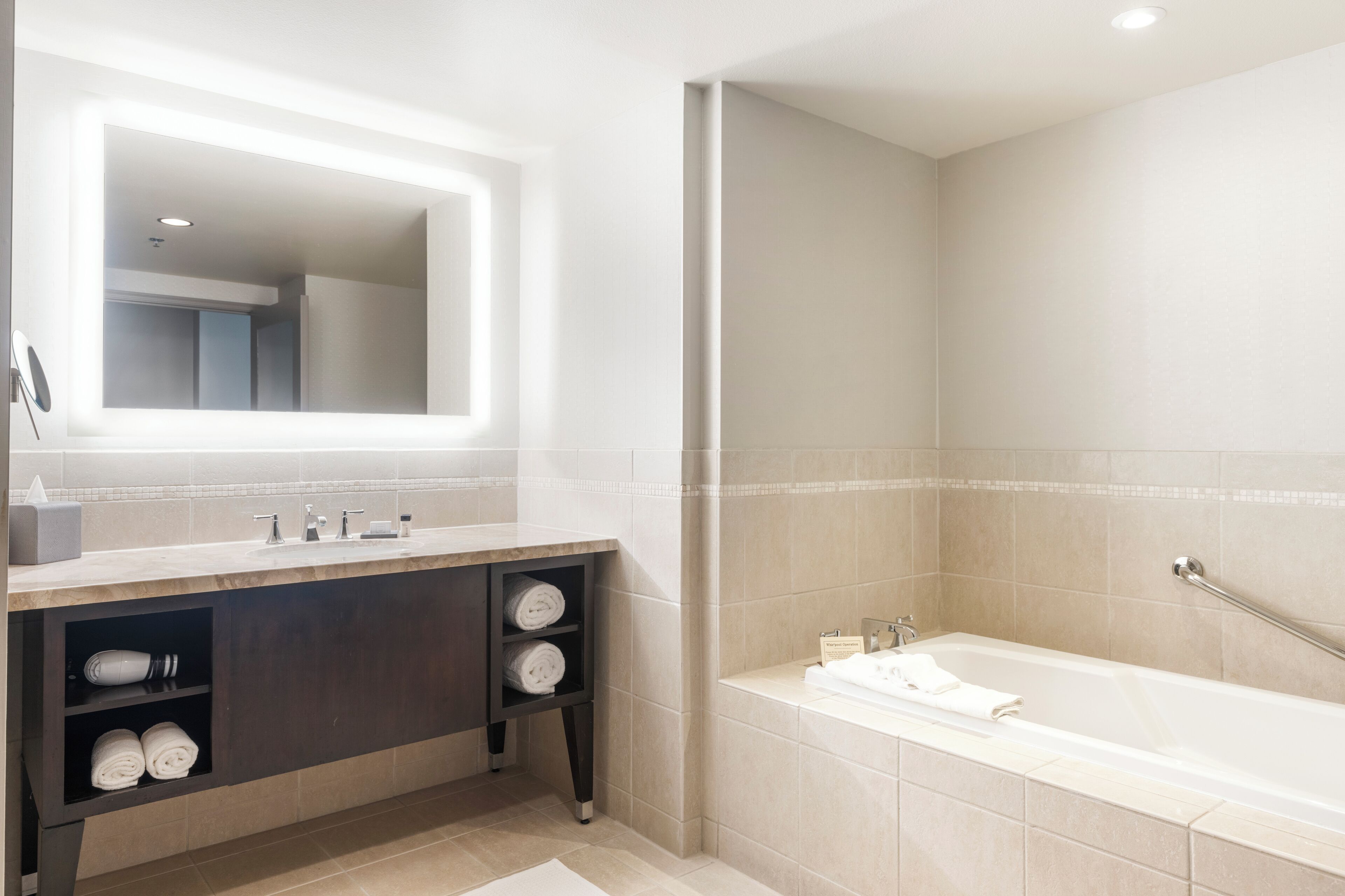 A modern bathroom with a large mirror, a bathtub, and a vanity with shelves.