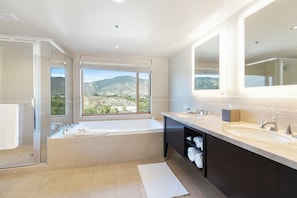 A modern bathroom with a large bathtub, two sinks, and a glass shower enclosure.