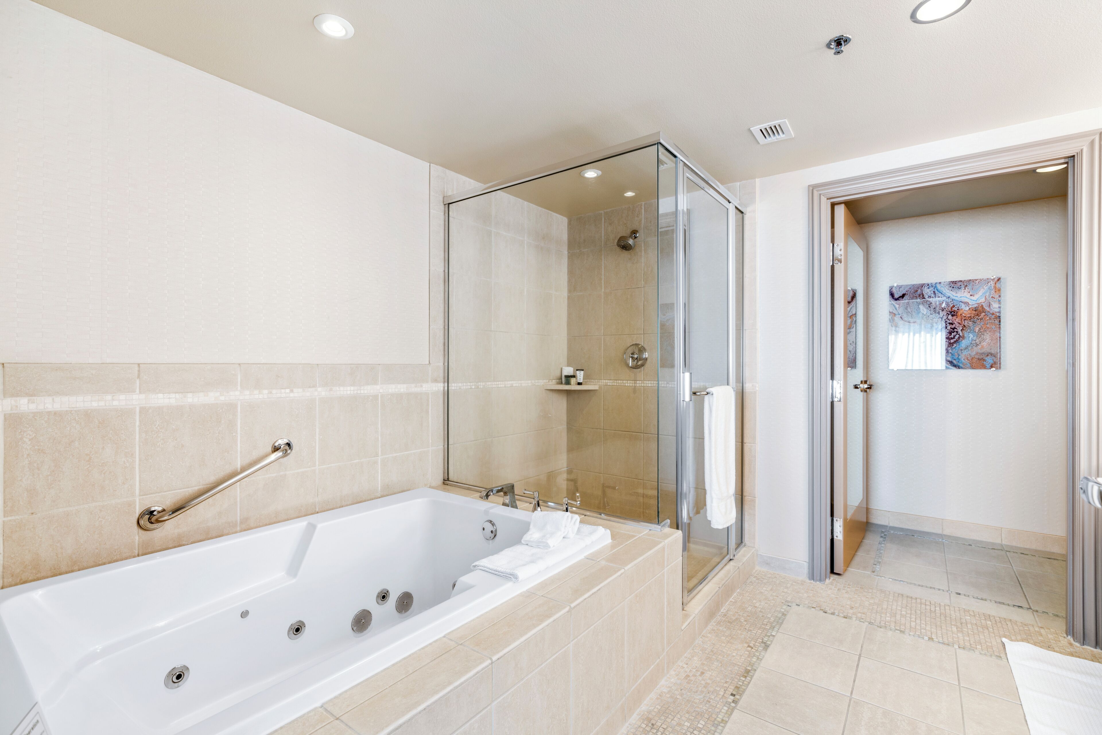 A modern bathroom with a glass-enclosed shower, a large bathtub, and a handrail.
