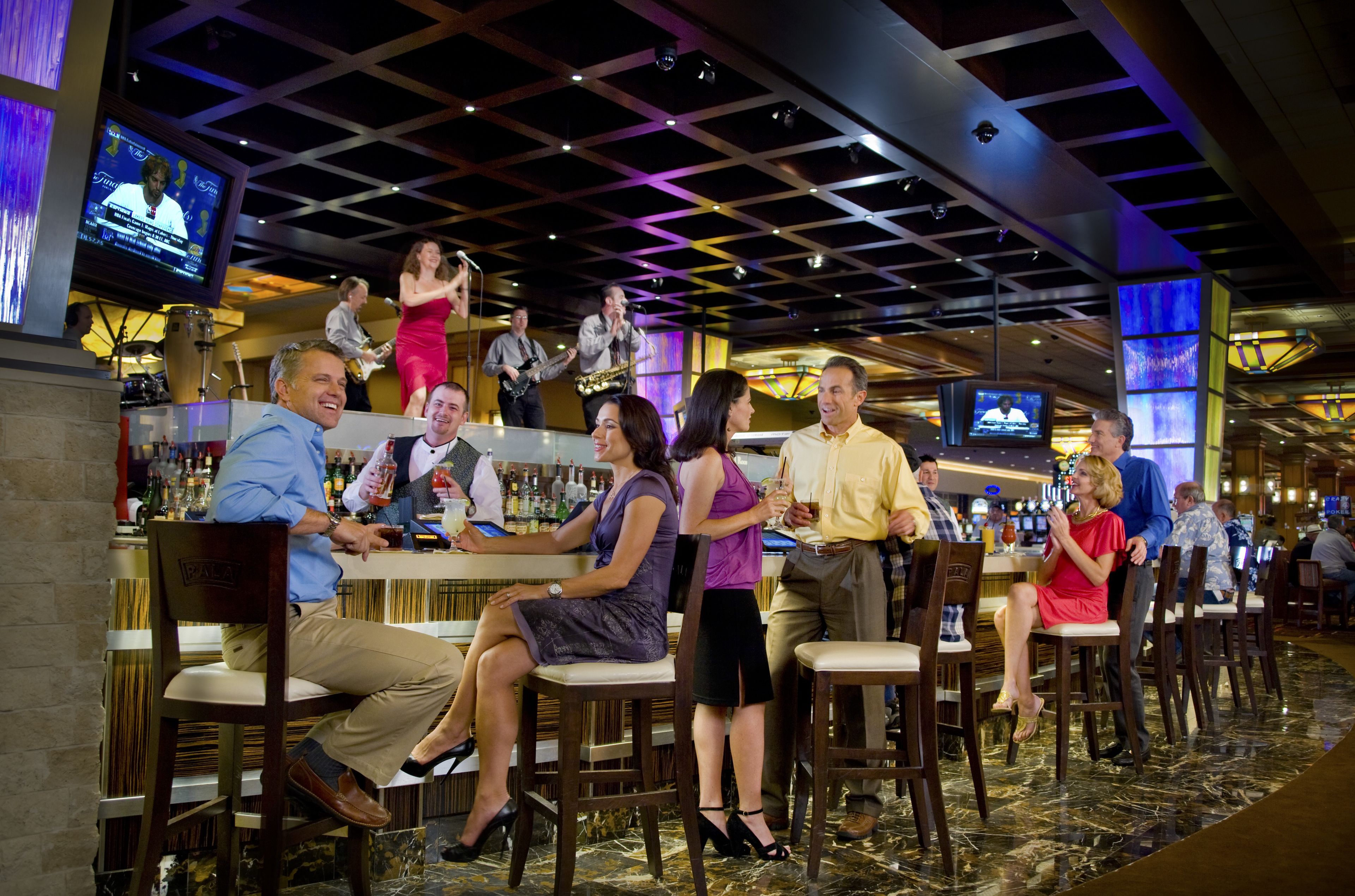 A bar area with multiple seating arrangements, a stage for performances, and a television screen displaying a news program.