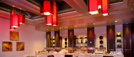 Un restaurante con barra libre, sillas blancas y lámparas colgantes rojas.