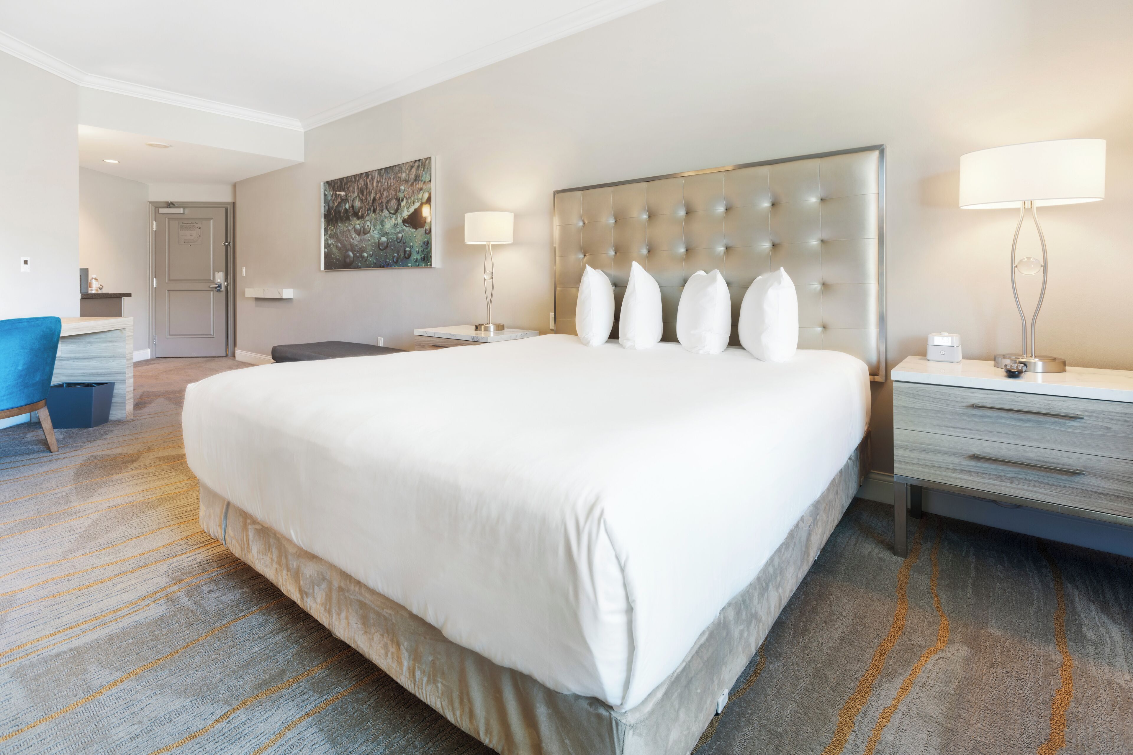 Una habitación de hotel con una cama grande, un escritorio, una silla y un cuadro en la pared.