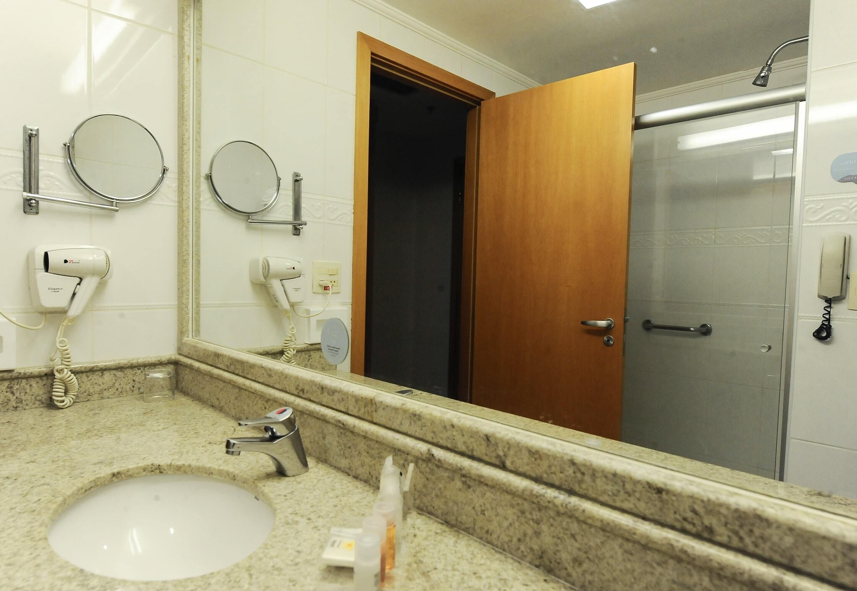 A bathroom with a sink, two mirrors, a hairdryer, and a shower.