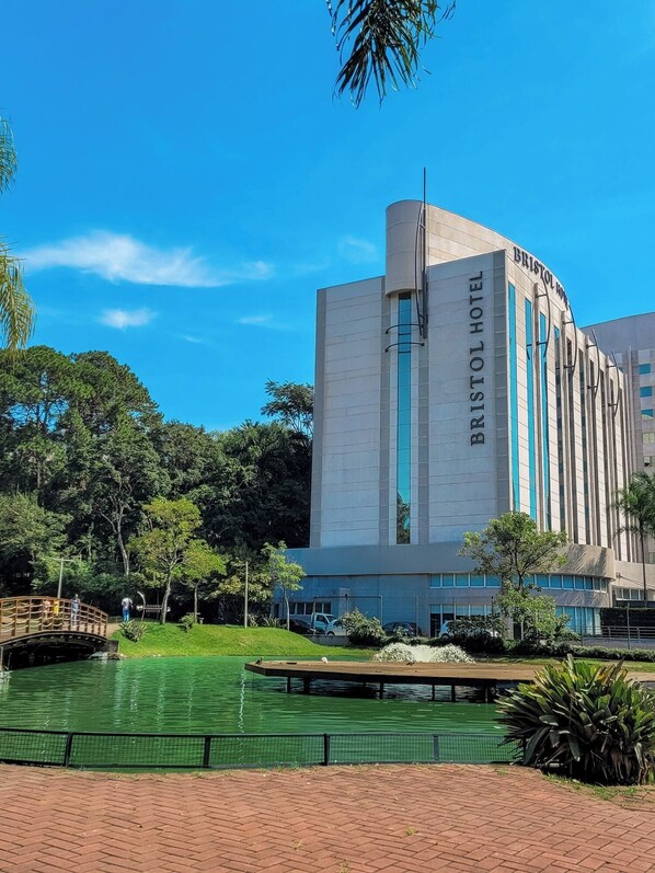 Un hotel moderno con un cartel llamativo, un jardín ajardinado y una fuente de agua.