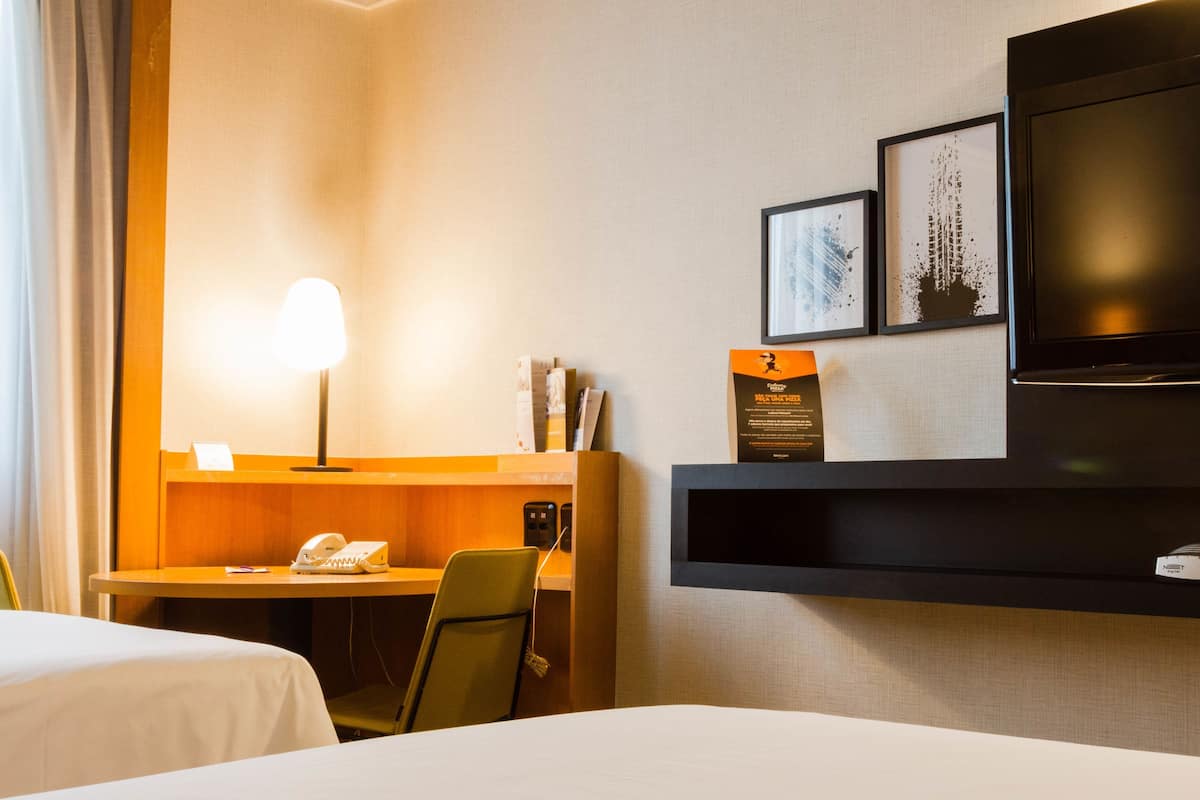 Une chambre d’hôtel équipée d’un lit, d’un bureau avec une lampe, d’un téléphone et d’un téléviseur fixé au mur.