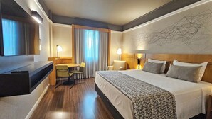 A hotel room with a large bed, a desk with a chair, a TV, and a wall with a geometric design. - Bristol Santo André Hotel (Santo André)
