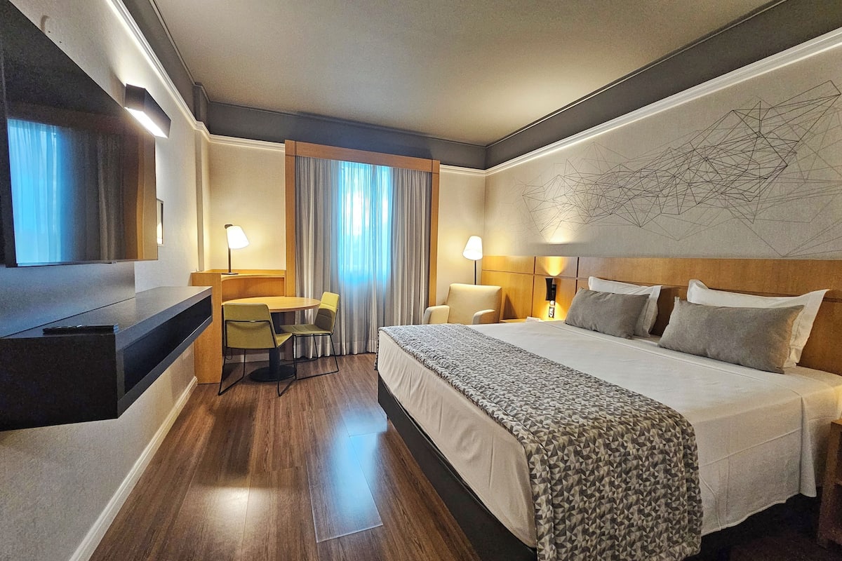 Une chambre d’hôtel avec un grand lit, un bureau avec une chaise, une télévision et un mur orné d’un motif géométrique.