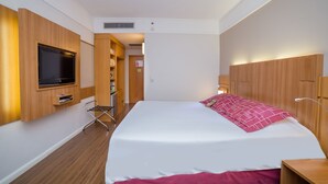 A hotel room with a large bed, wooden wardrobe, a TV mounted on the wall, and a small seating area. - Bristol Santo André Hotel (Santo André)