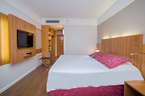 Habitación de hotel con una cama grande, armario de madera, televisor montado en la pared y una pequeña zona de estar.
