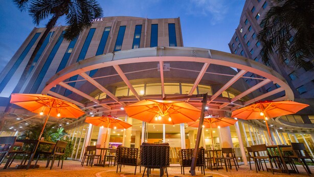 An outdoor seating area with tables and chairs under large umbrellas, in front of a building with a curved glass facade.