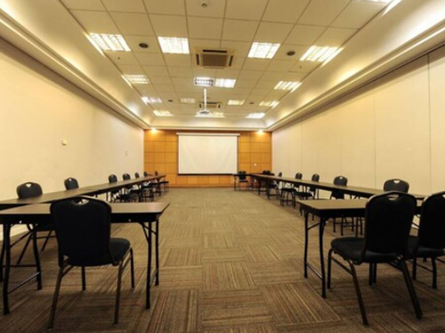 Una sala de conferències amb una pantalla gran al capdavant, diverses taules amb cadires i un paviment amb moqueta.