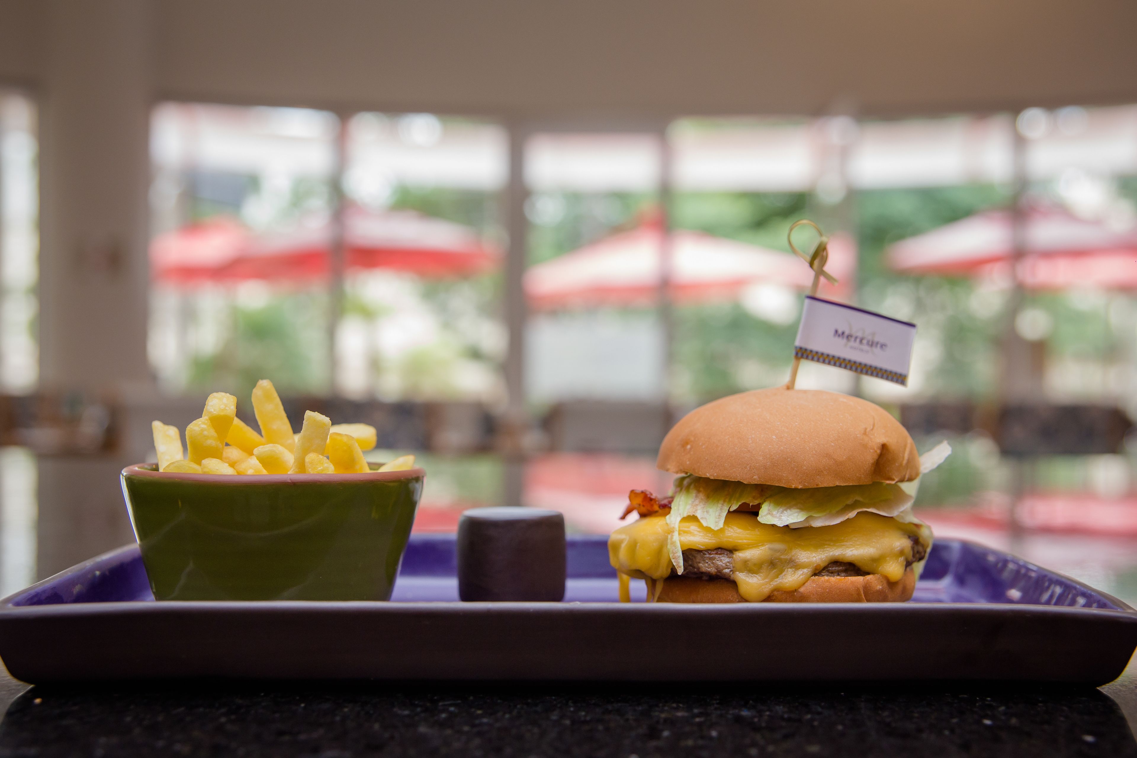 A tray with a burger and fries on a table in a restaurant with large windows and red umbrellas in the background.