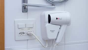 Un baño con secador de pelo, espejo, dispensador de toallas y tendedero para toallas.
