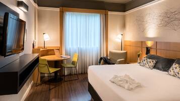 Ein Hotelzimmer mit Bett, Schreibtisch, Stuhl, Fernseher und einem Fenster mit Vorhängen.