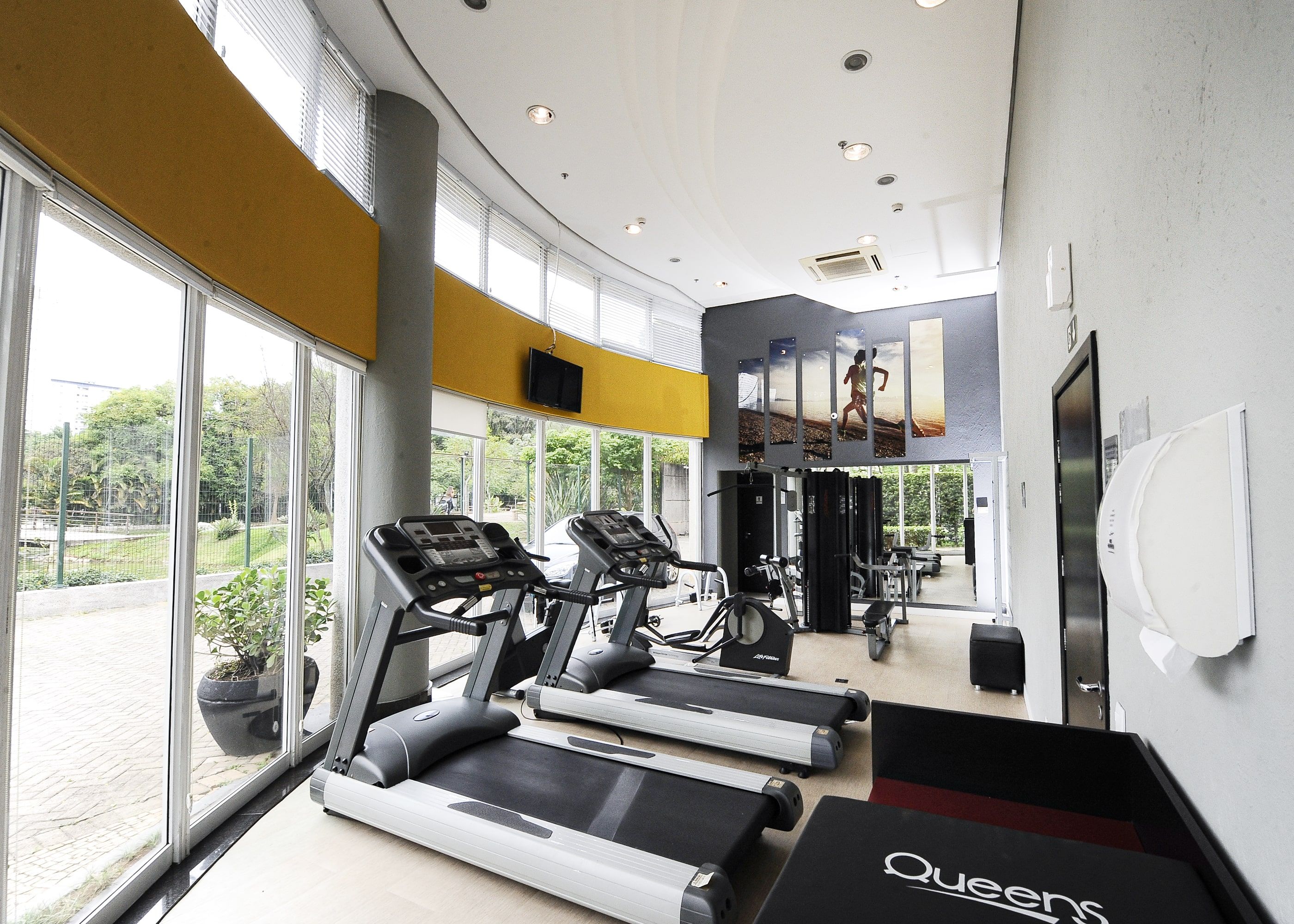 Un gimnasio con cintas de correr, equipamiento de ejercicio y ventanas amplias que dan a la naturaleza.