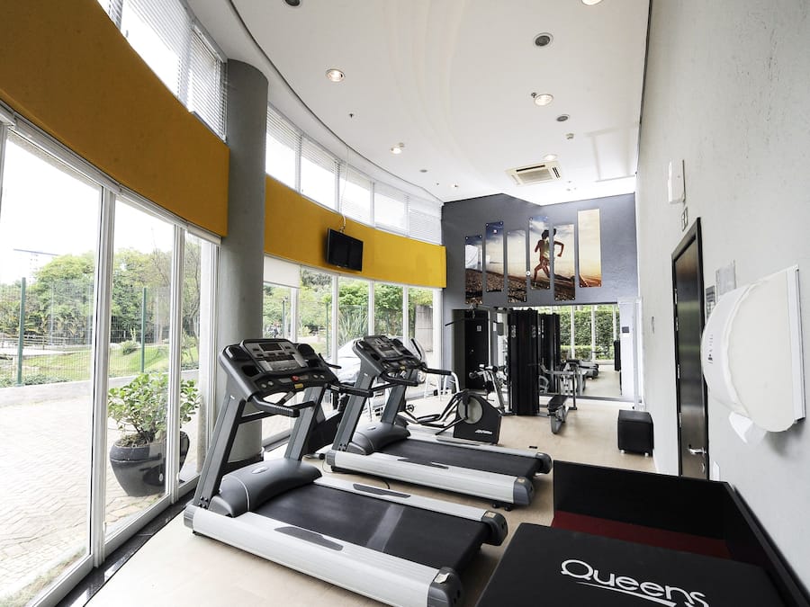 Academia com esteiras, equipamentos de ginástica e amplas janelas que proporcionam vista para o exterior.
