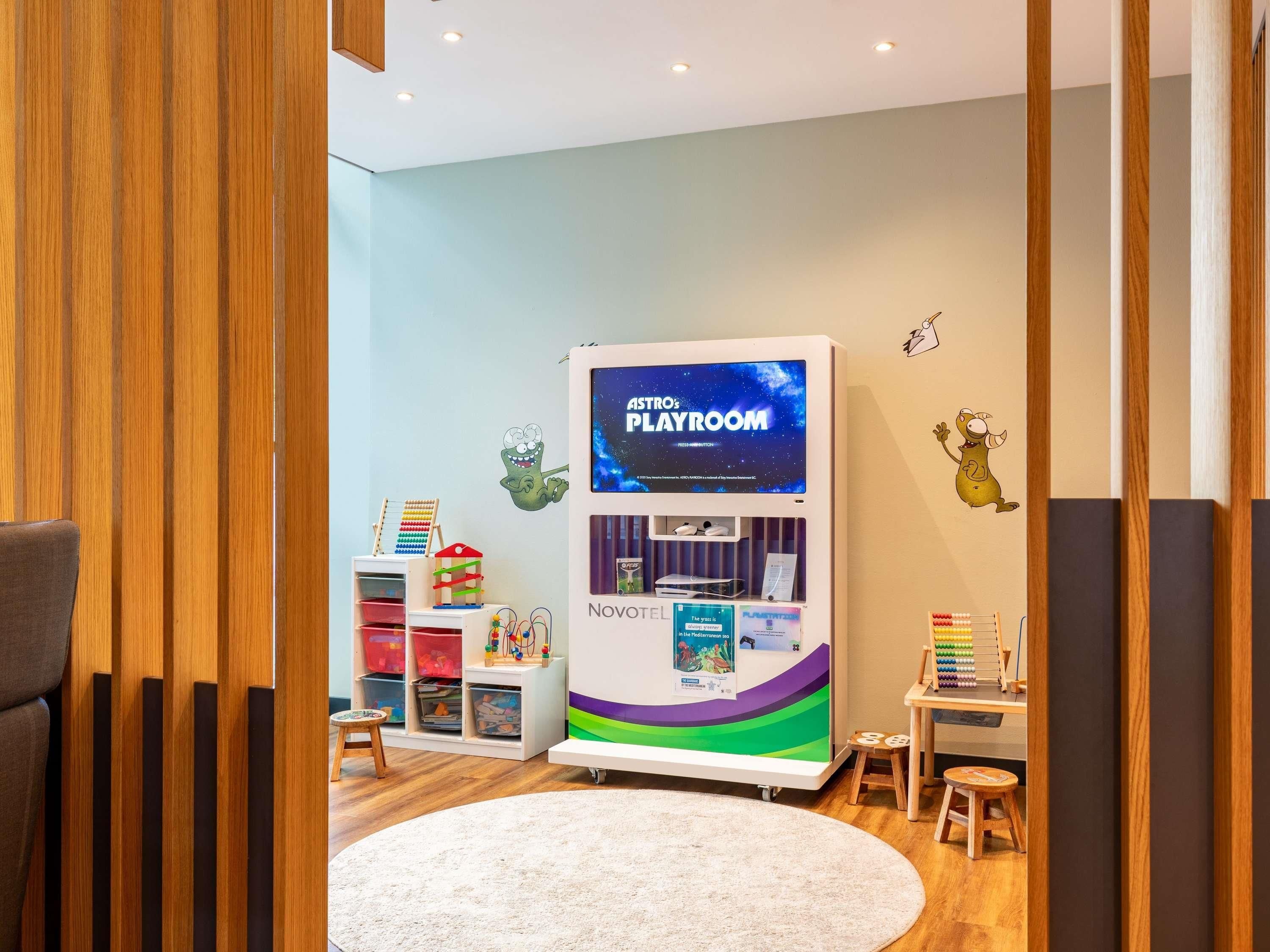 Ein Kinderspielzimmer mit einem NOVOTEL Spielbereich, Holzboden und einem weißen Teppich.