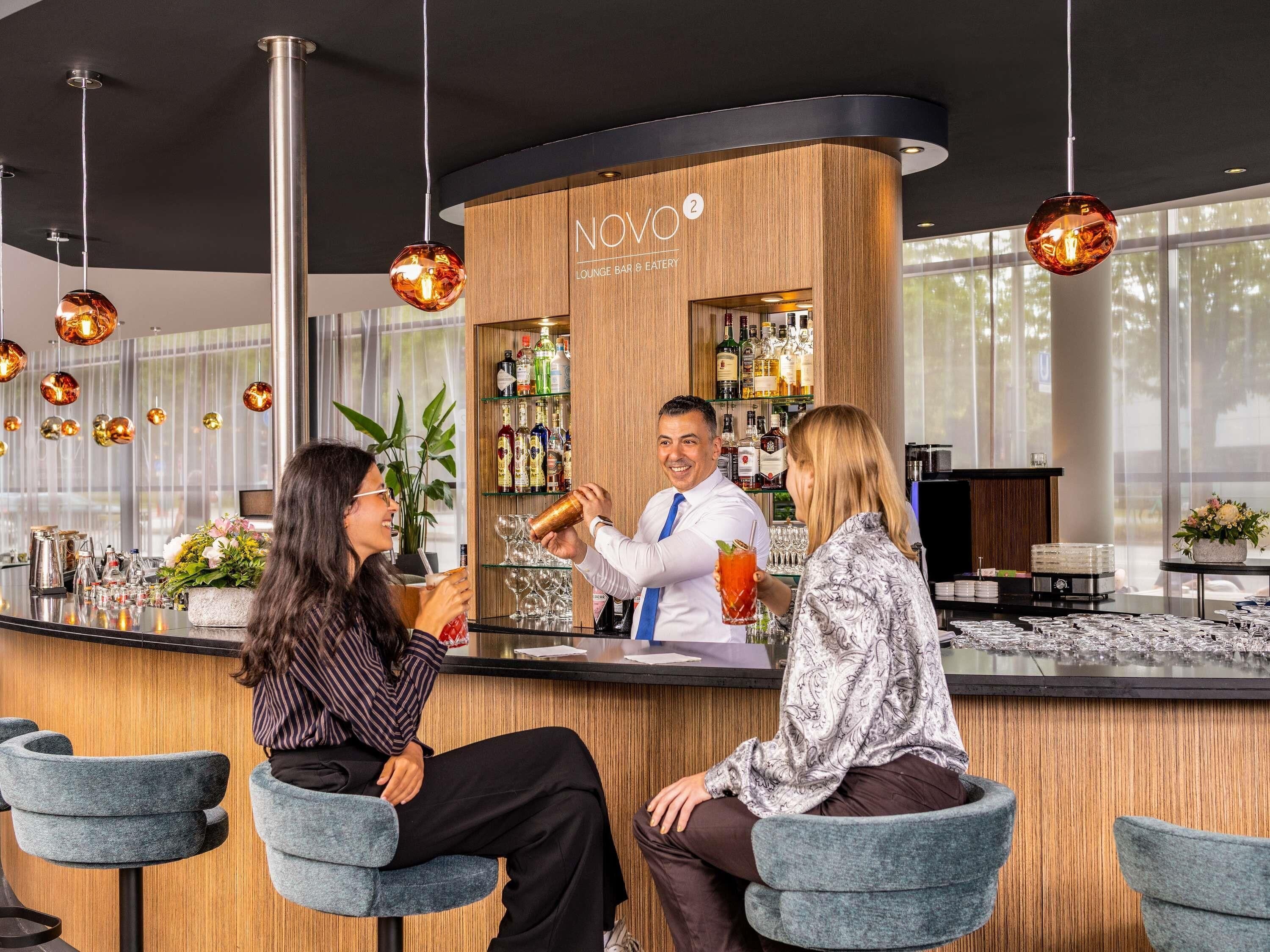 A bar area with a wooden counter, bar stools, and hanging pendant lights.