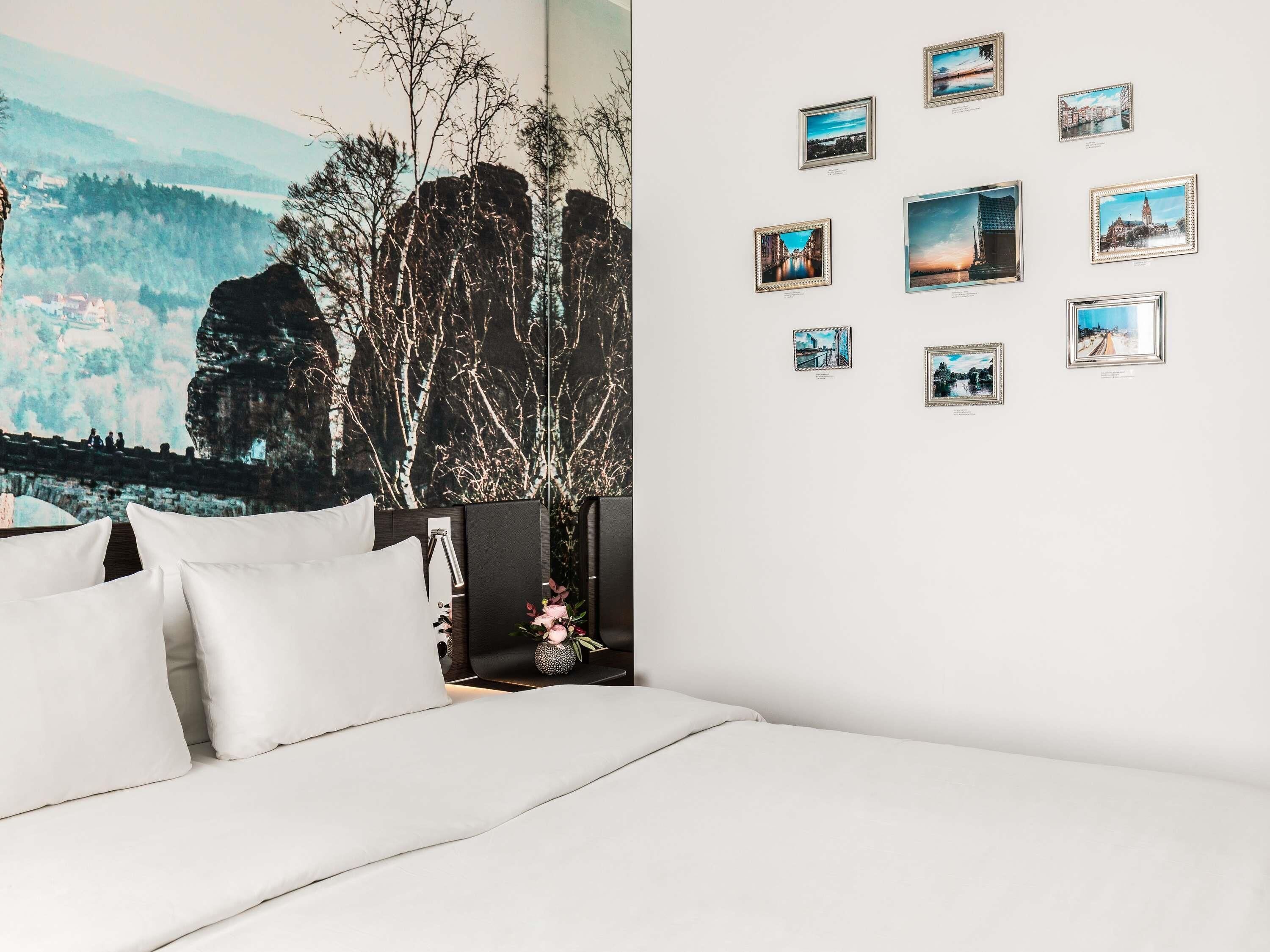 A bedroom with a large bed, a wall with framed pictures, and a mural of a landscape.