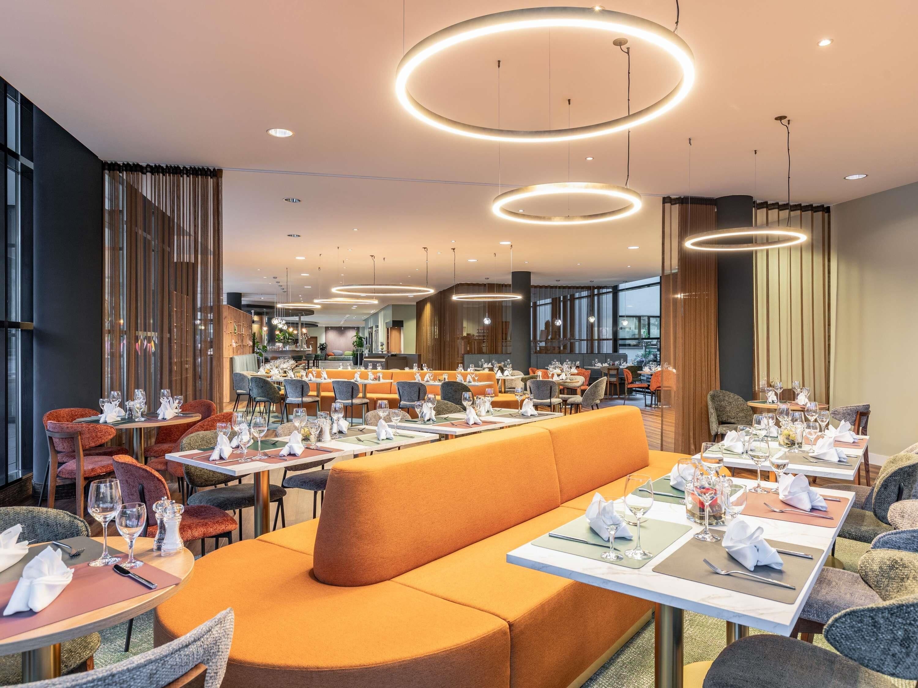 Un restaurante moderno con varias zonas de comedor, incluyendo un área central con asientos tipo banca naranja y mesas individuales.