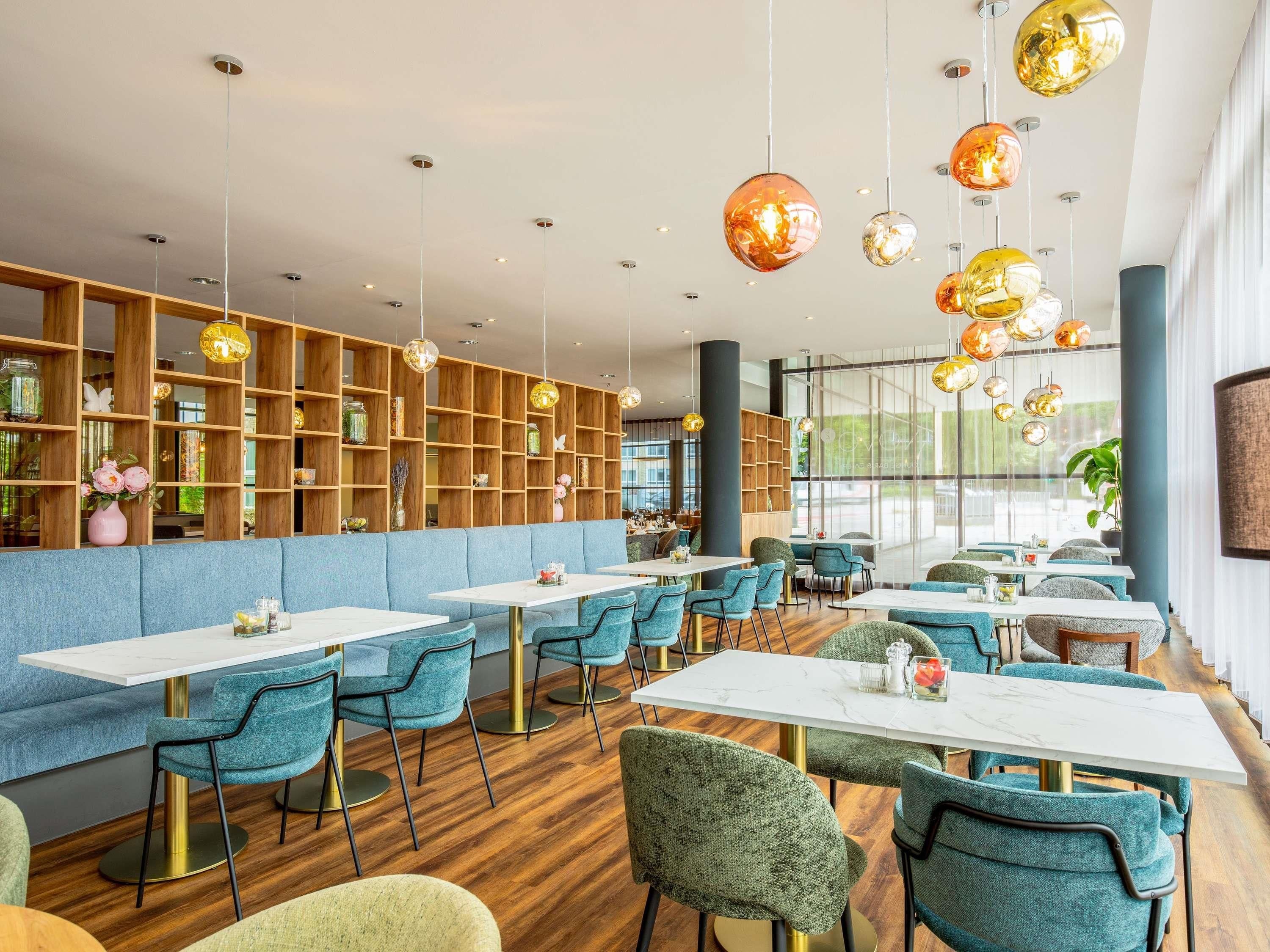 A modern dining area with wooden shelves, blue upholstered seating, and pendant lighting.
