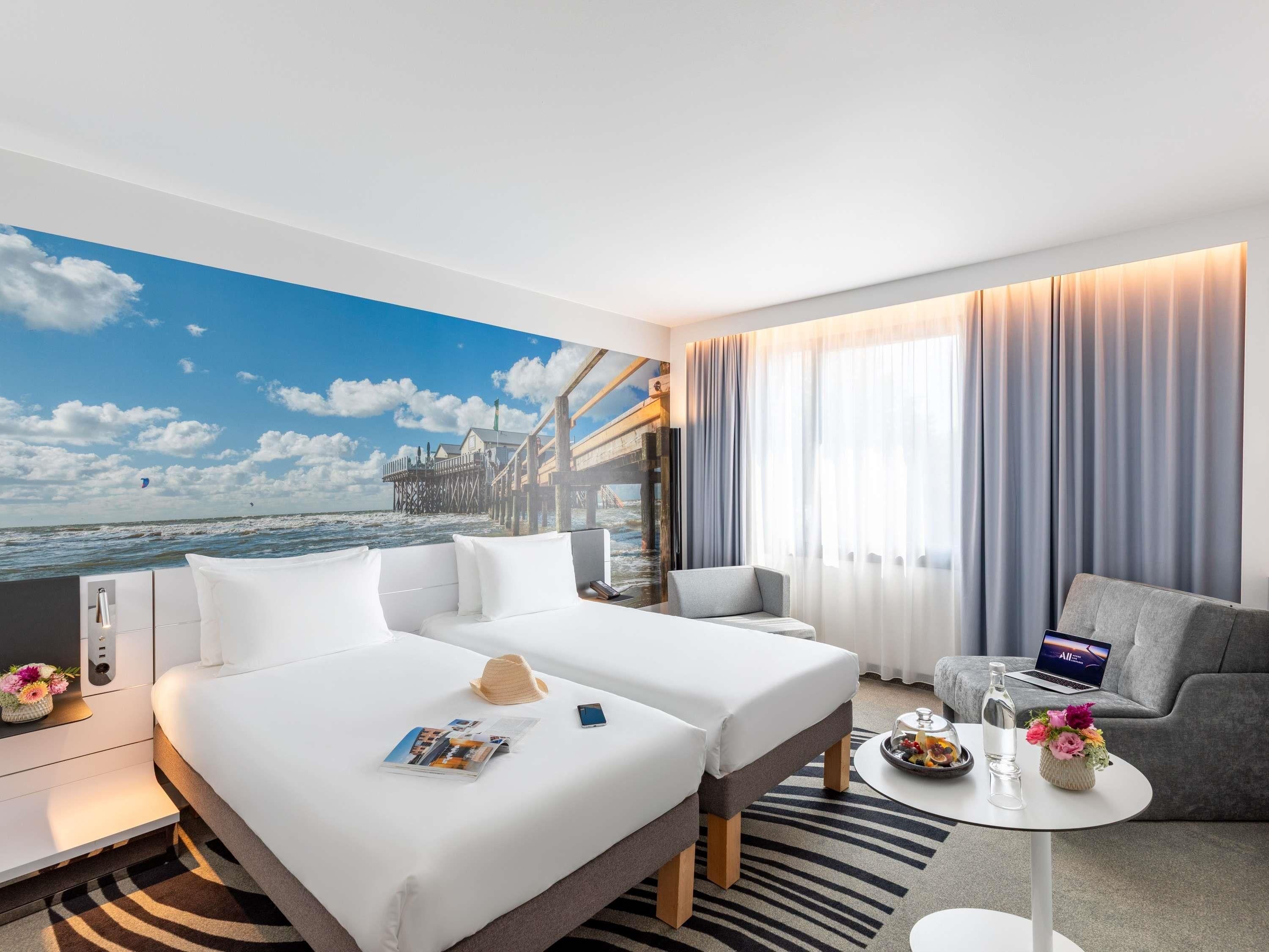 A hotel room with a bed, a sofa, a small table, and a view of a pier.