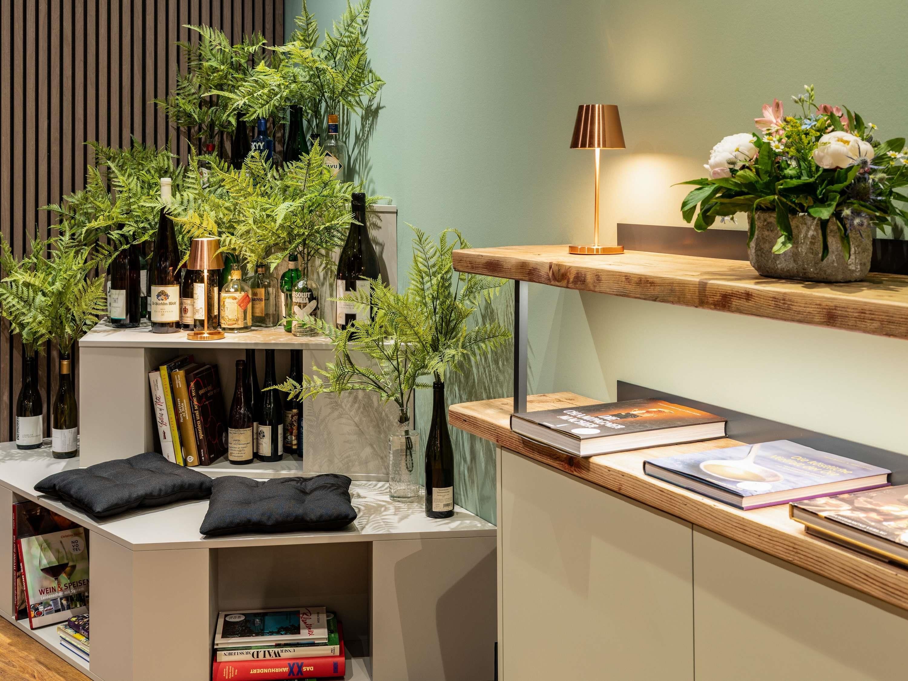 Un interior moderno con una estantería, botellas de vino, una lámpara y un arreglo floral.