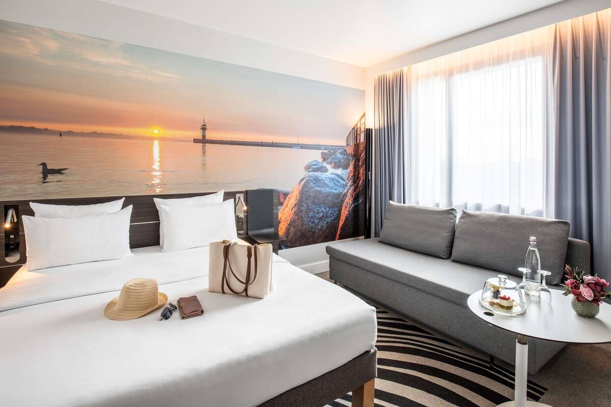 Une chambre d’hôtel avec un lit, un canapé, une petite table et une vue sur le coucher de soleil au-dessus de l’eau.