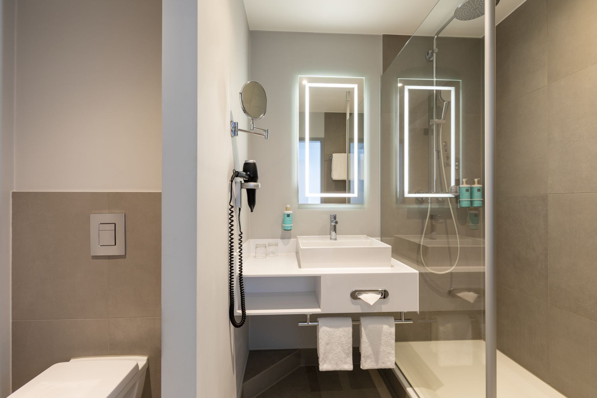 A modern bathroom with a white sink, a mirror, and a glass-enclosed shower.