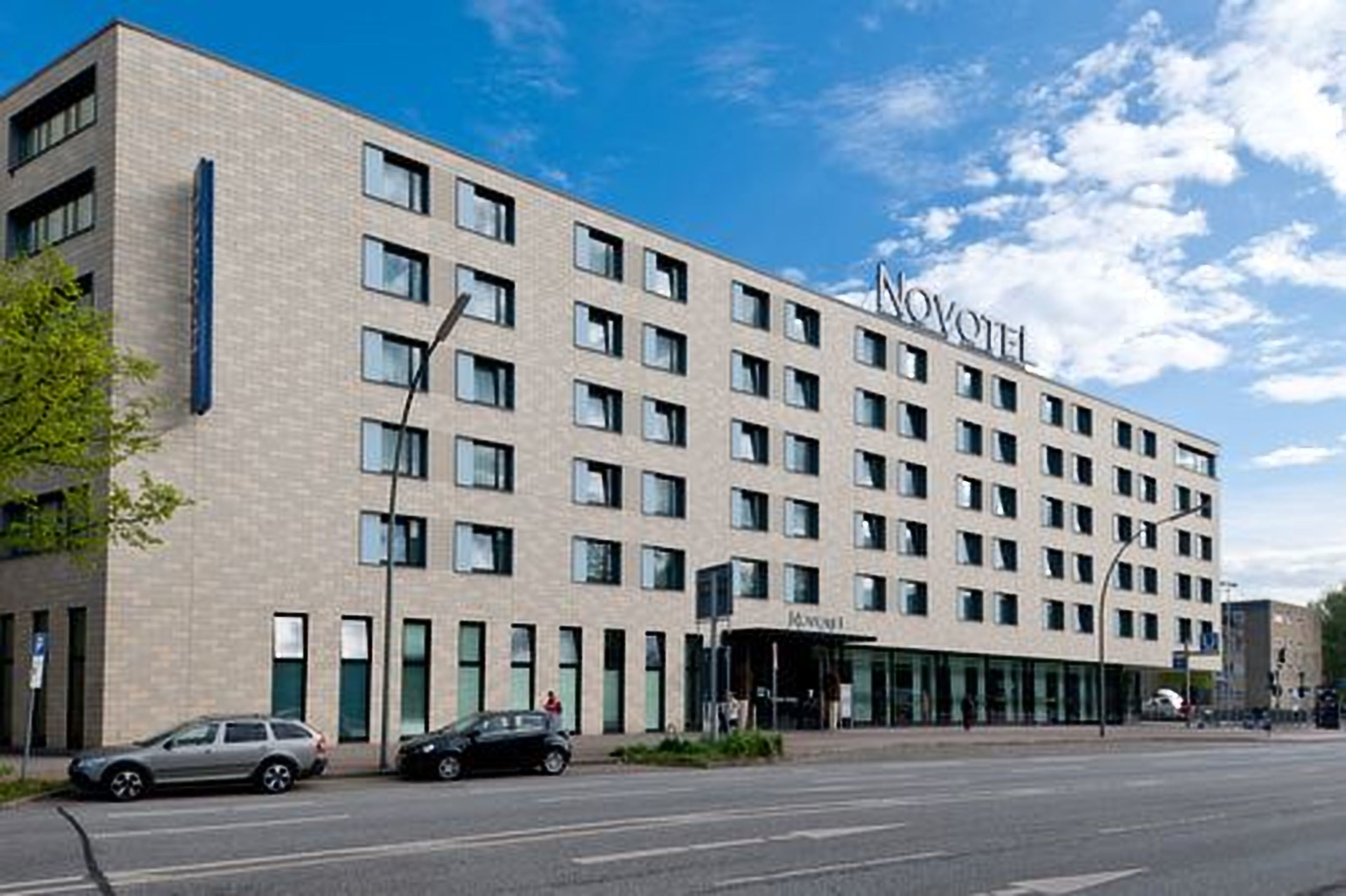 A modern hotel building with a flat facade, multiple windows, and a prominent "NOVOMILE" sign.