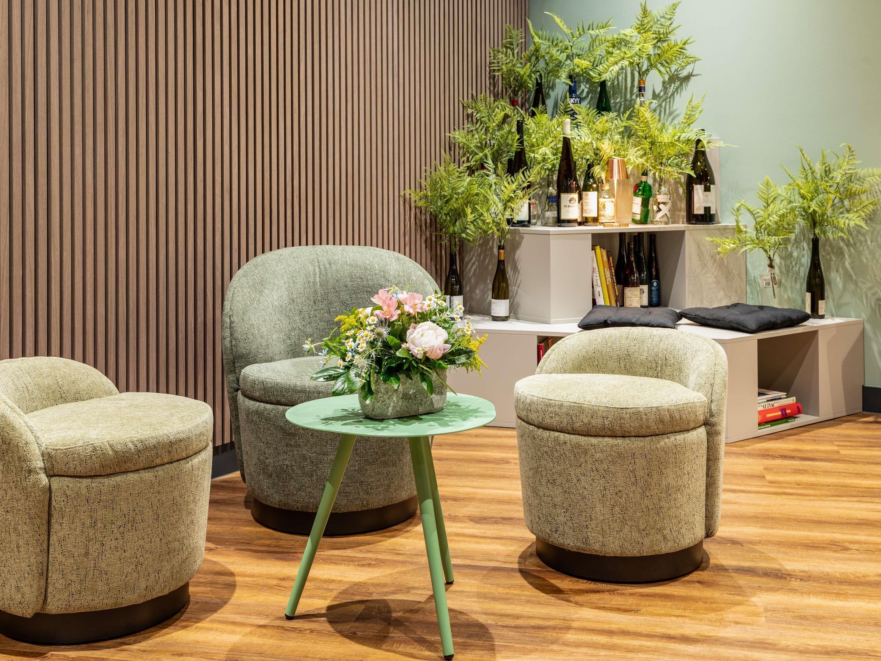 A modern interior with two armchairs, a small round table with a flower arrangement, and a bookshelf filled with wine bottles.