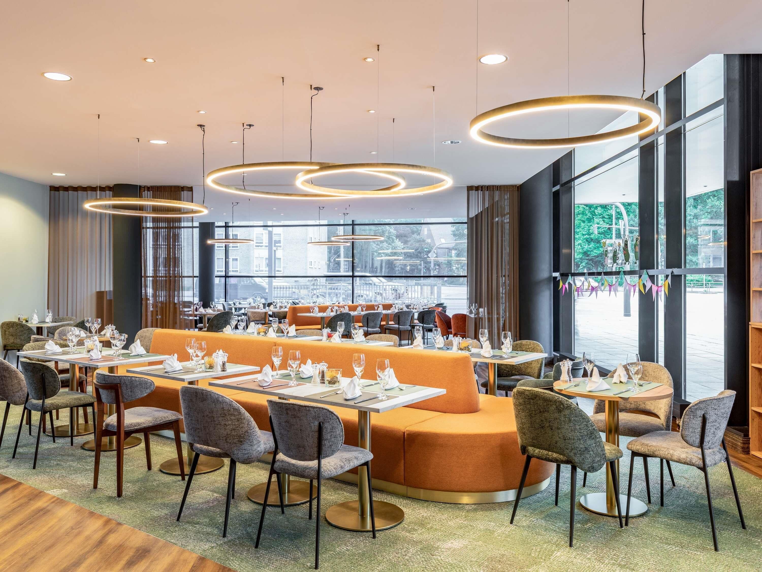 Un restaurante moderno con mesas redondas, asientos naranjas y amplios ventanales que ofrecen vistas a la calle.