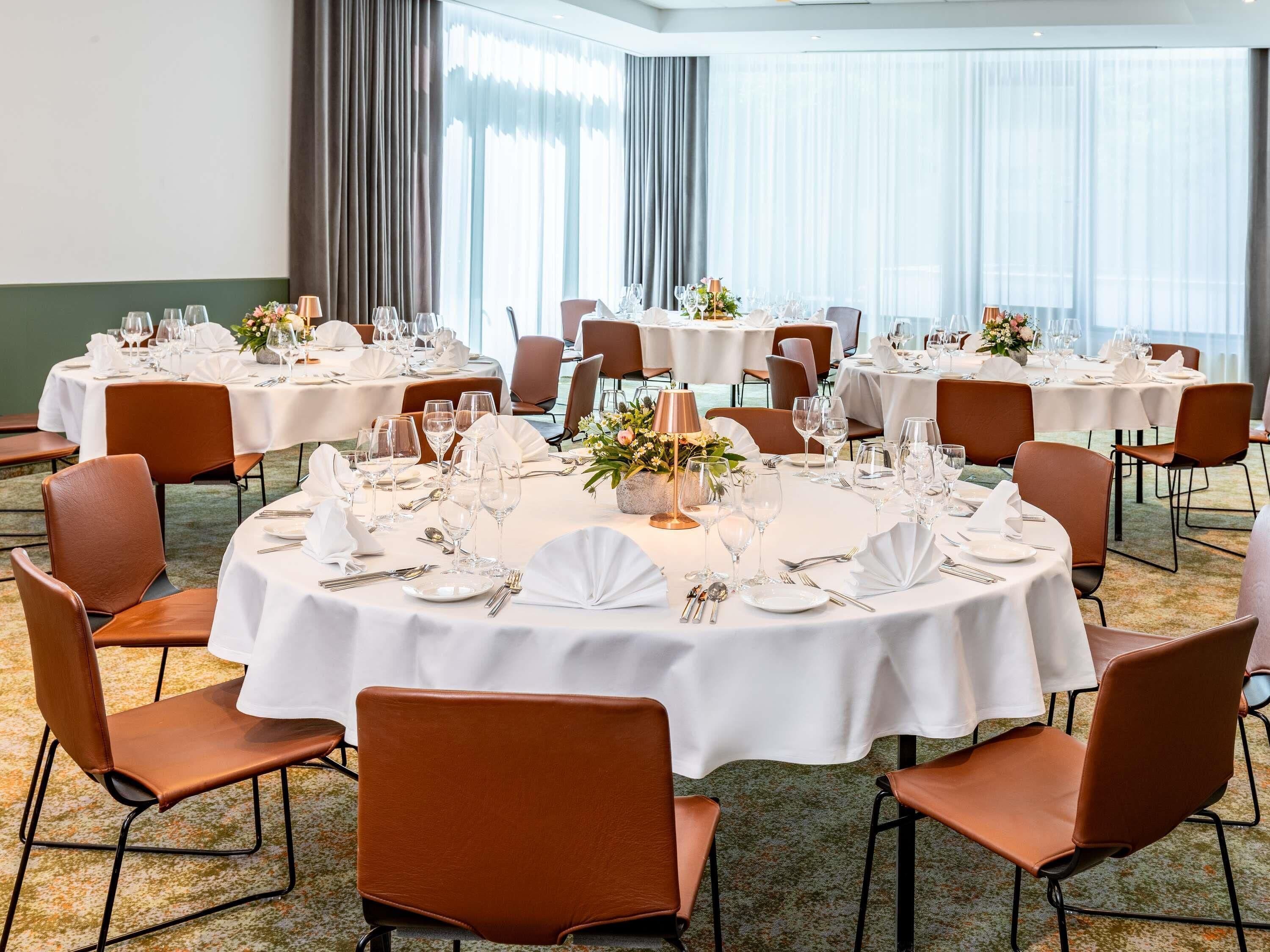 A hotel dining area with round tables, brown leather chairs, and white tablecloths.
