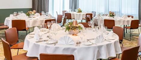 A hotel dining area with round tables, brown leather chairs, and white tablecloths.