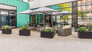 Un espace extérieur aménagé en terrasse, avec des tables et des chaises, entouré de jardinières remplies de plantes vertes.