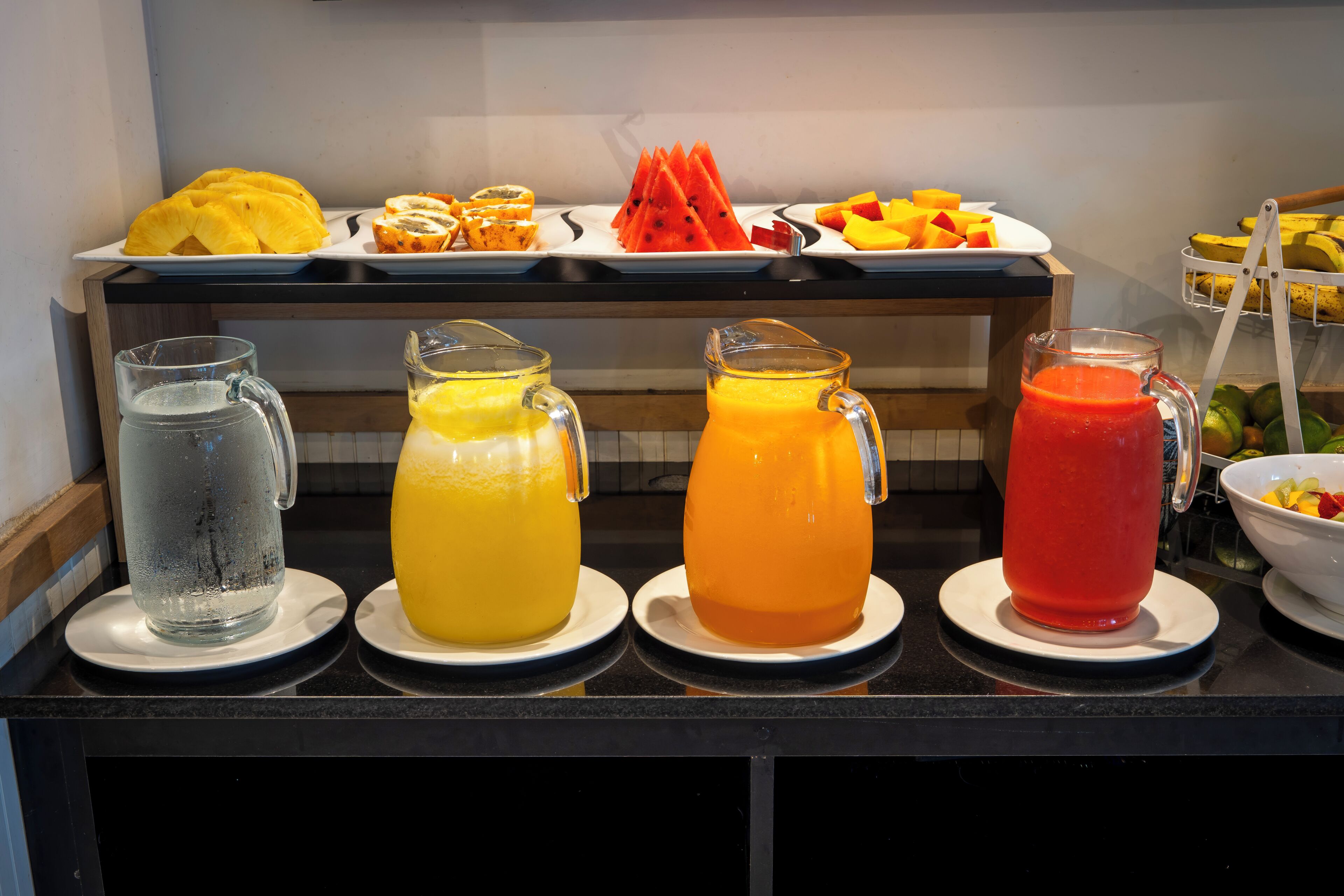 A buffet table with various fruit options and three pitchers of different colored beverages.