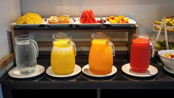 Una mesa de buffet con diversas opciones de fruta y tres jarras de bebidas de colores distintos.