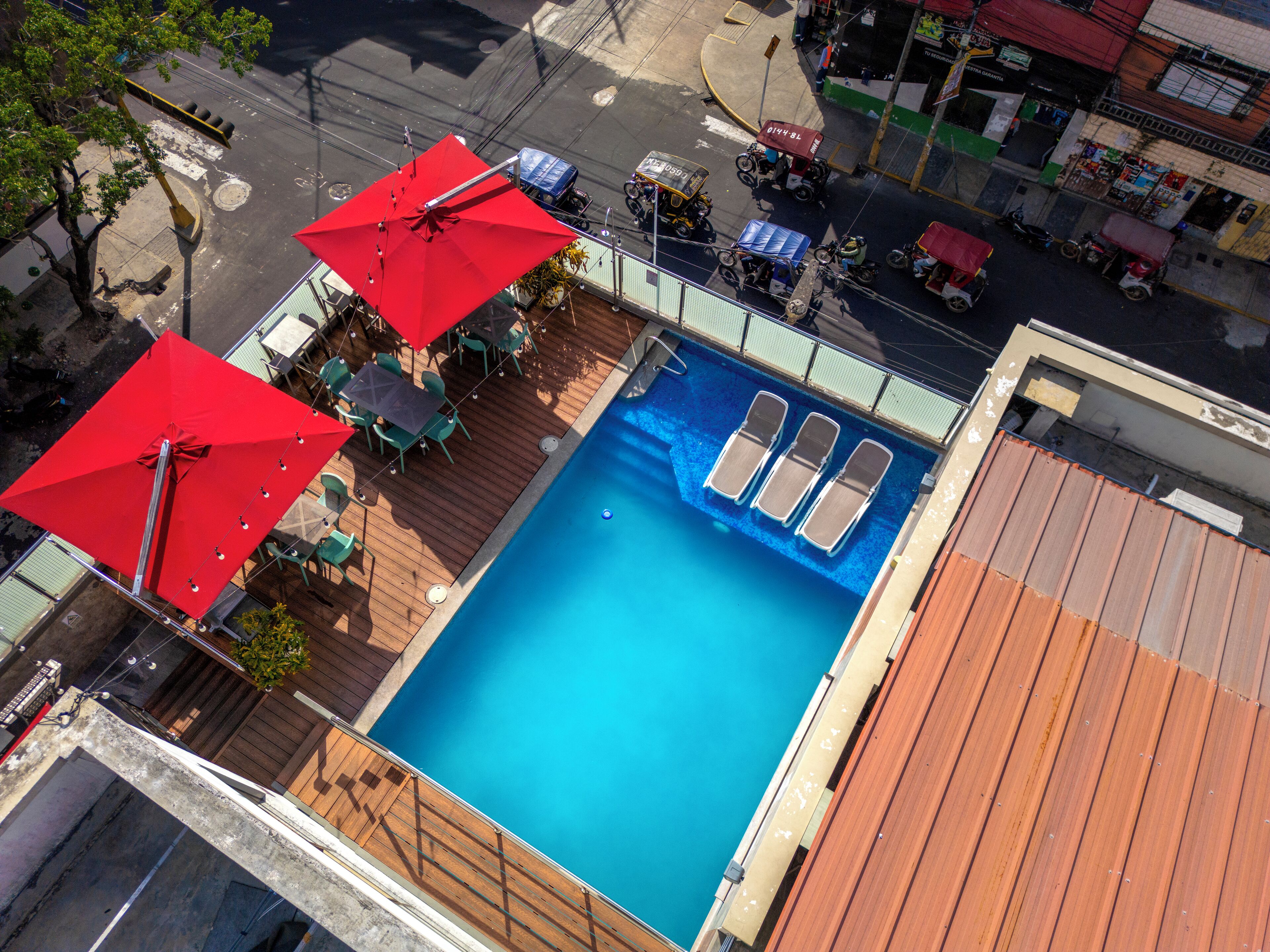 Una piscina en la azotea con tres tumbonas y dos sombrillas rojas.