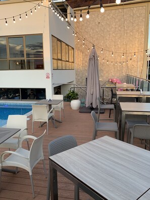 An outdoor patio area with tables and chairs, string lights, a pool, and a stone wall. - Victoria Regia Hotel (Iquitos)