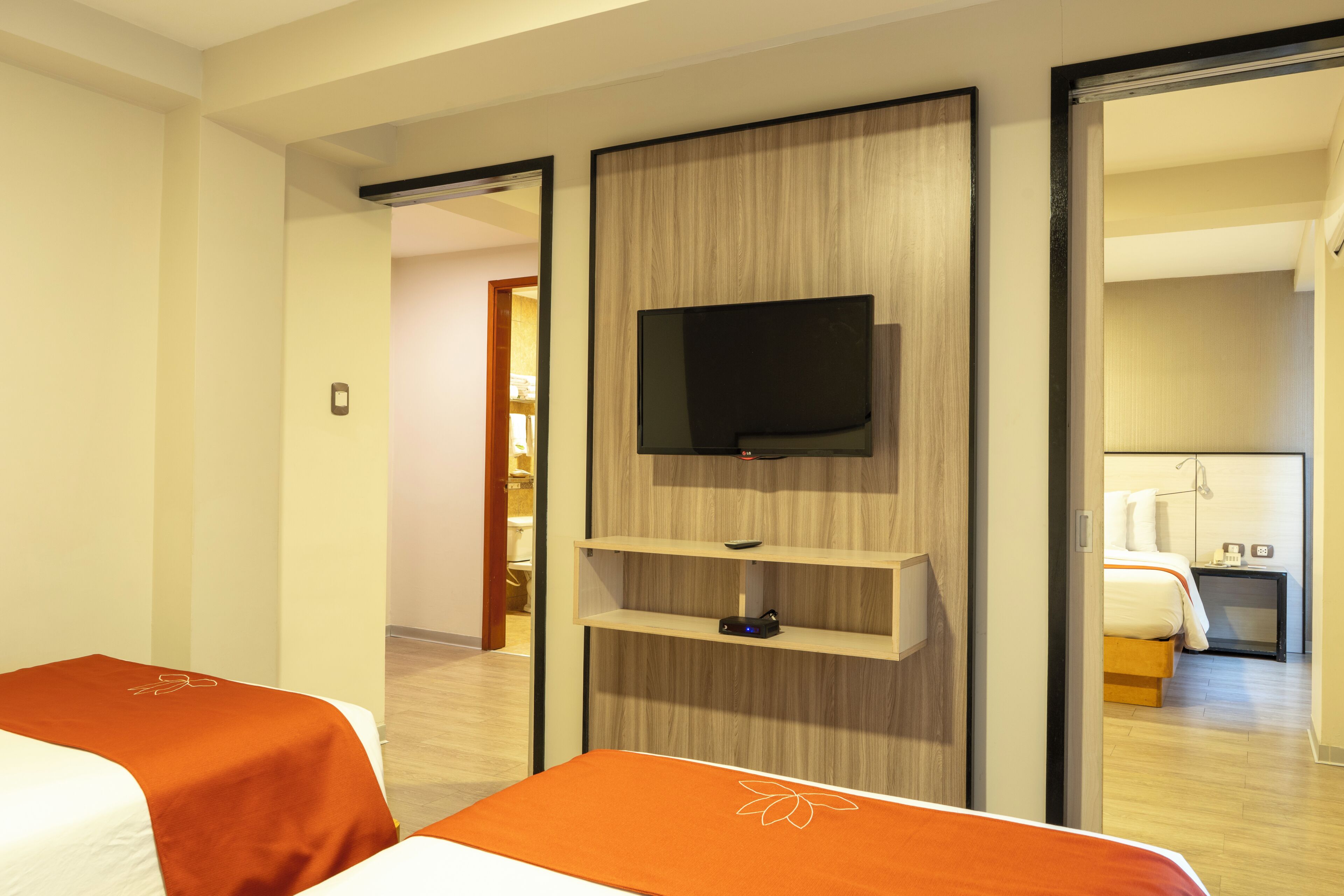 Ein Hotelzimmer mit einem Bett, einem an einer Holzplatte montierten Fernseher und einem Nachttisch mit Telefon und Lampe.