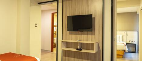 A hotel room with a bed, a TV mounted on a wooden panel, and a bedside table with a phone and a lamp.