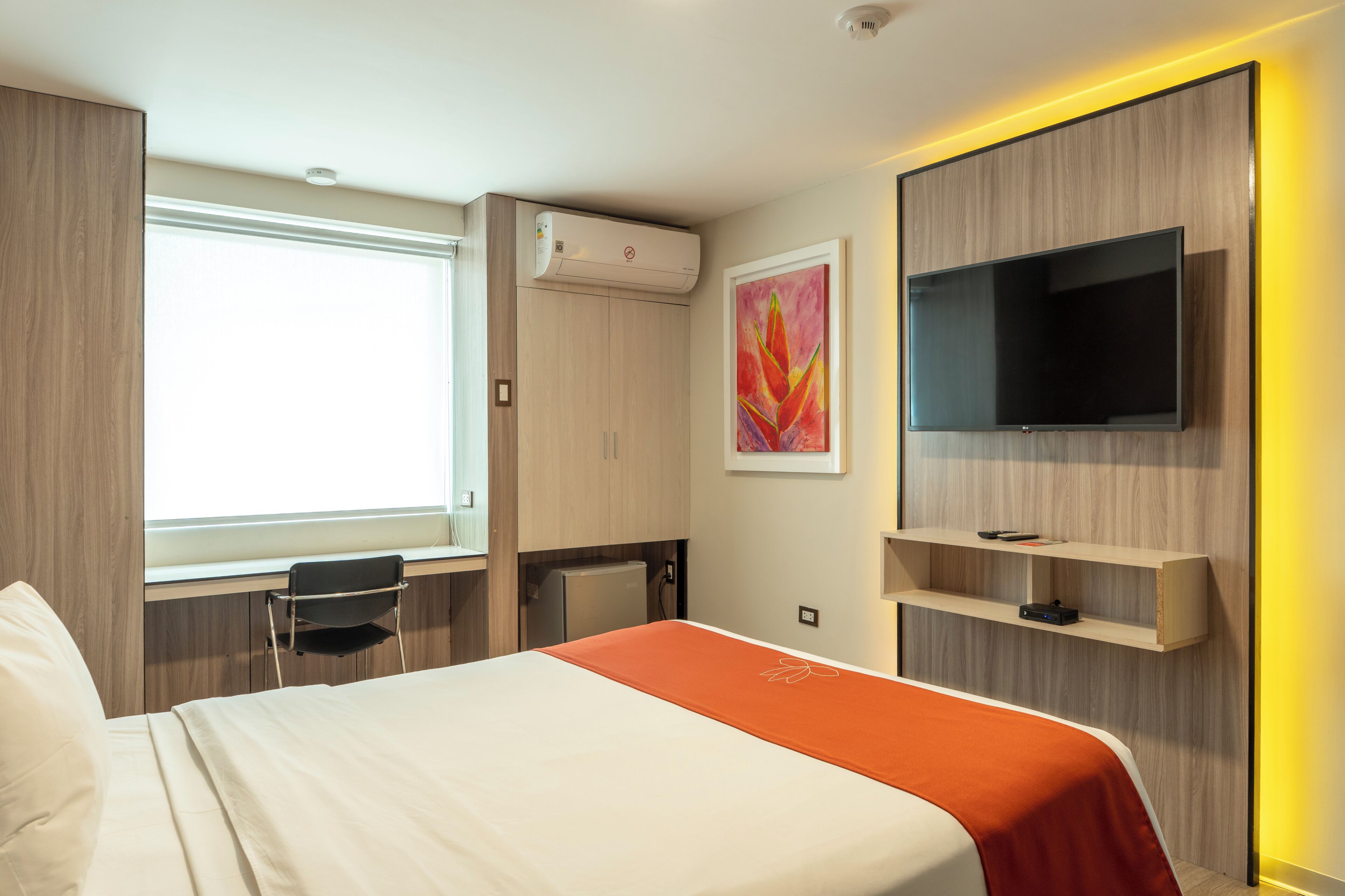 A hotel room with a bed, a desk, a chair, a television, and a window.