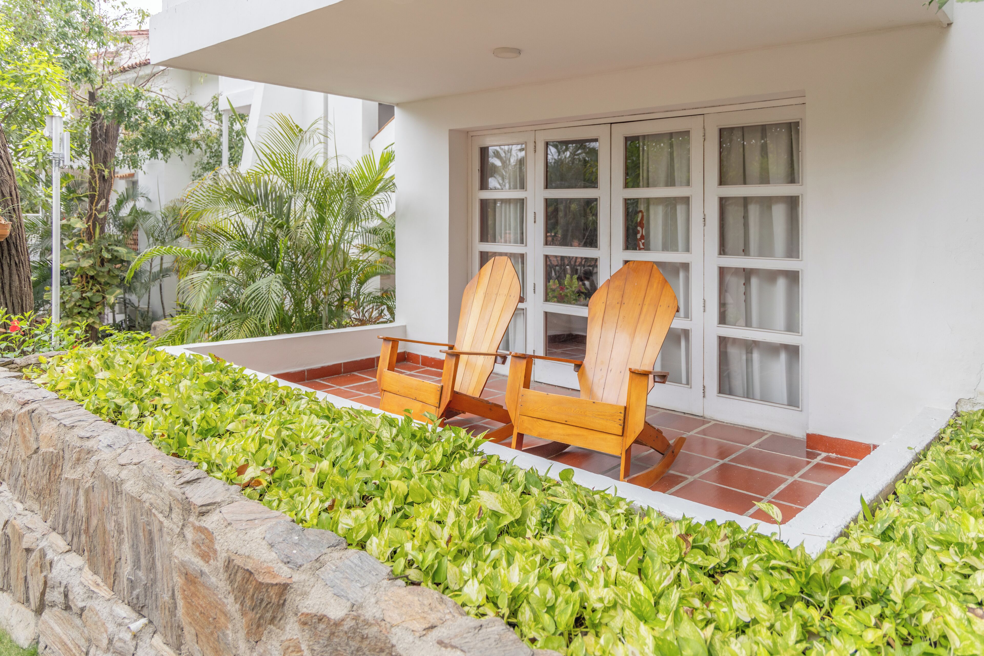 A patio with two wooden chairs and a stone wall.