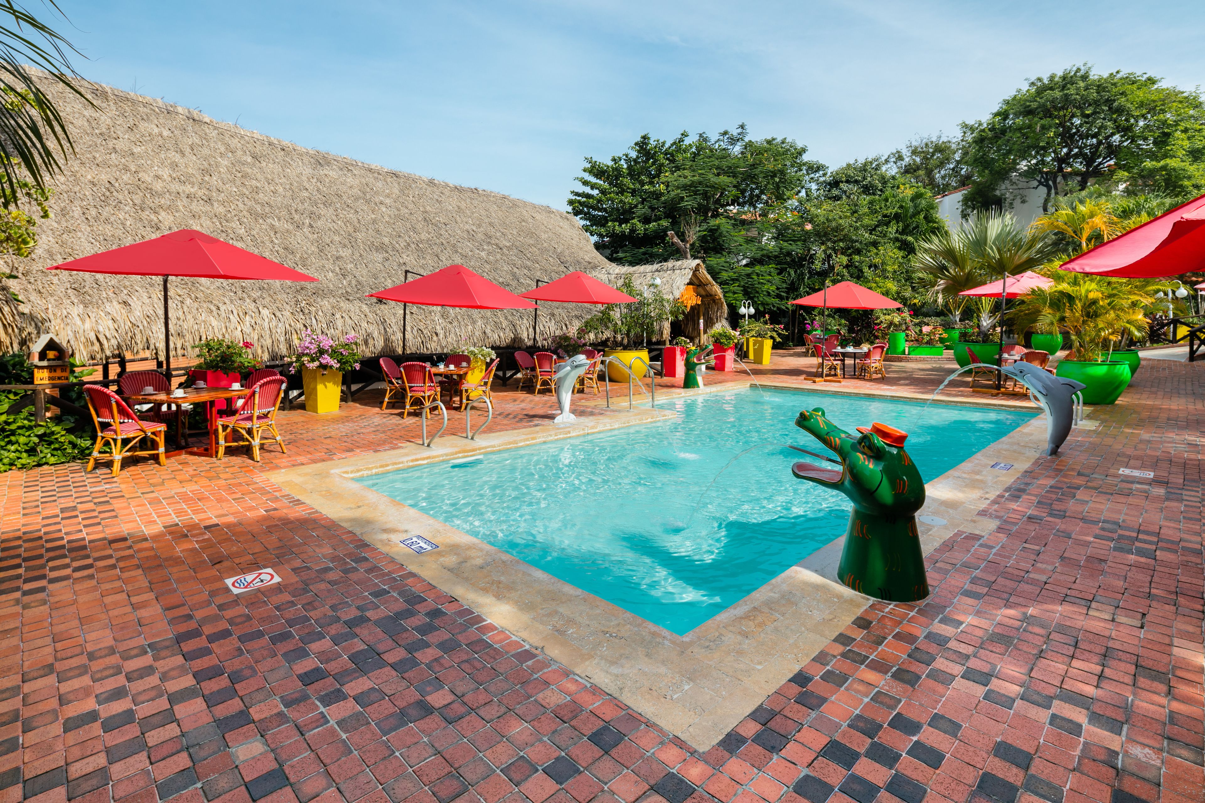 A pool area with red umbrellas, lounge chairs, and a brick floor.