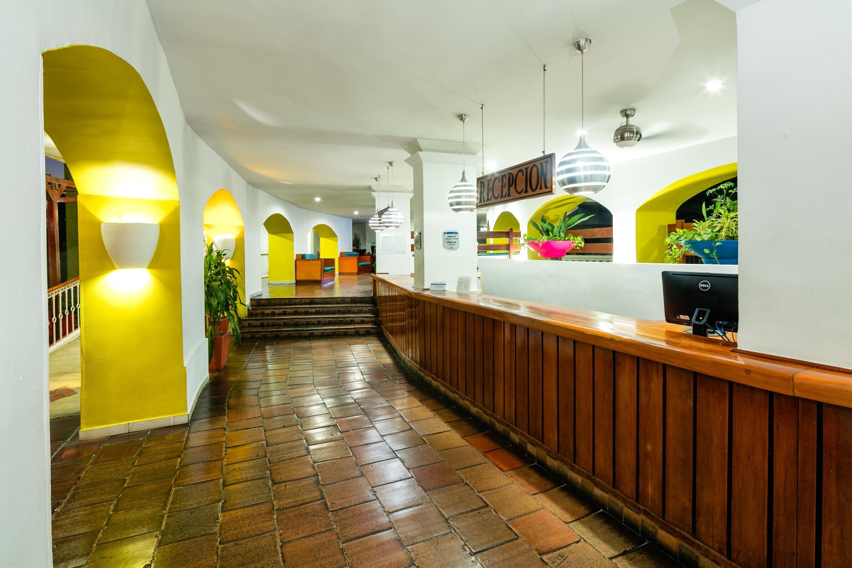 A hotel reception area with a wooden reception desk, a staircase leading to upper floors, and a sign indicating the reception.